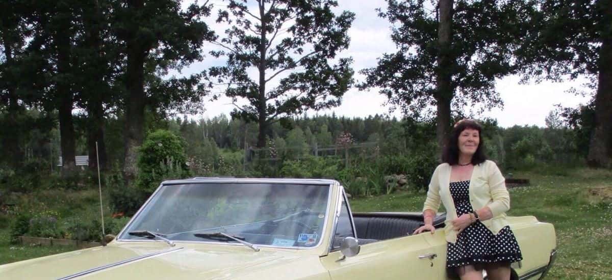 A classic Oldsmobile car with its top down. Ann, from Meet the Locals stands beside the car