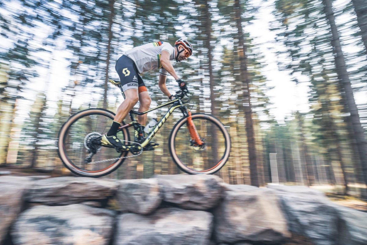 A man goes very fast over some rocks on his MTB bike. The photo is all blurry because he is going so fast